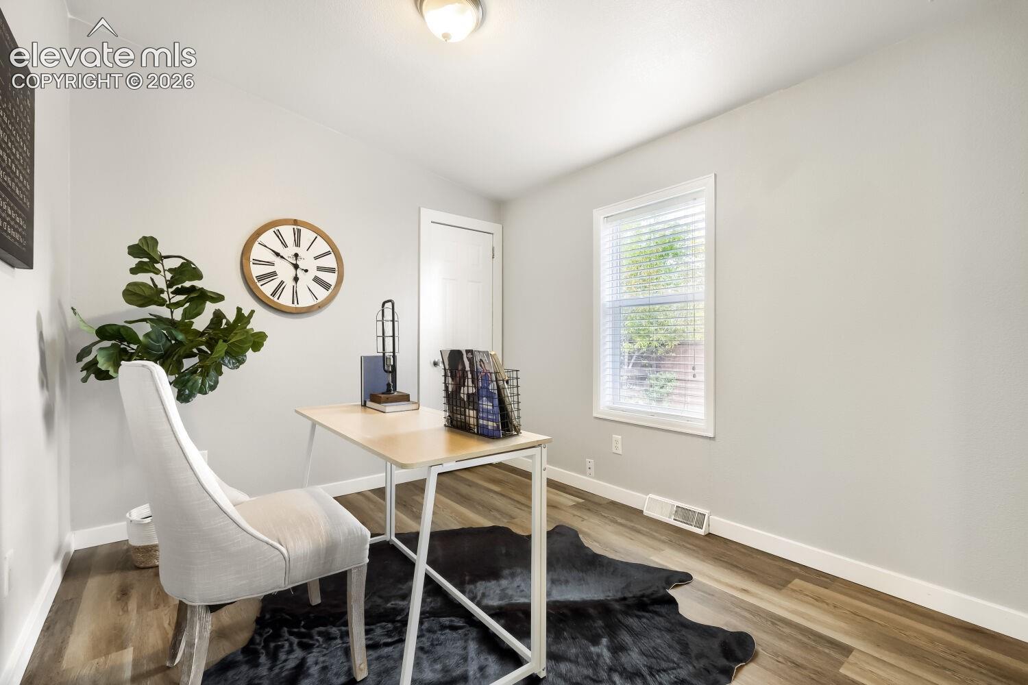 Room featuring neutral wall paint, wood-finish flooring, a flush-mount ceiling light fixture, and a window with horizontal blinds