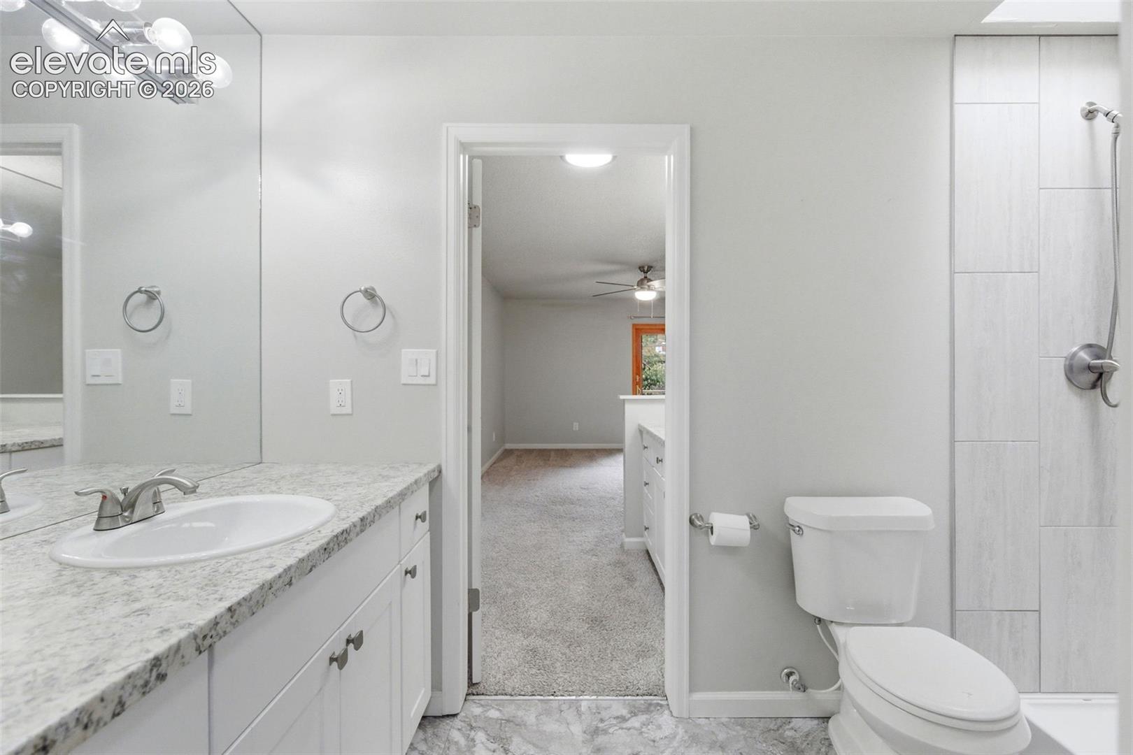 Bathroom featuring a shower with tiled surround, a white toilet, and a vanity with a white basin and speckled countertop
