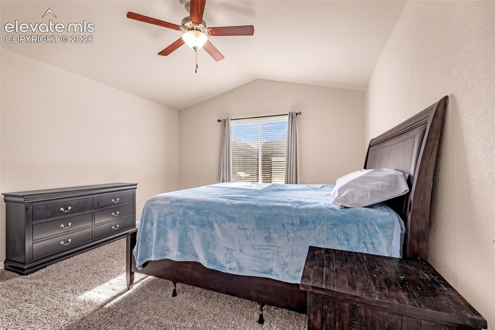 Vaulted ceiling with a ceiling fan, window with blinds, and neutral-toned wall paint