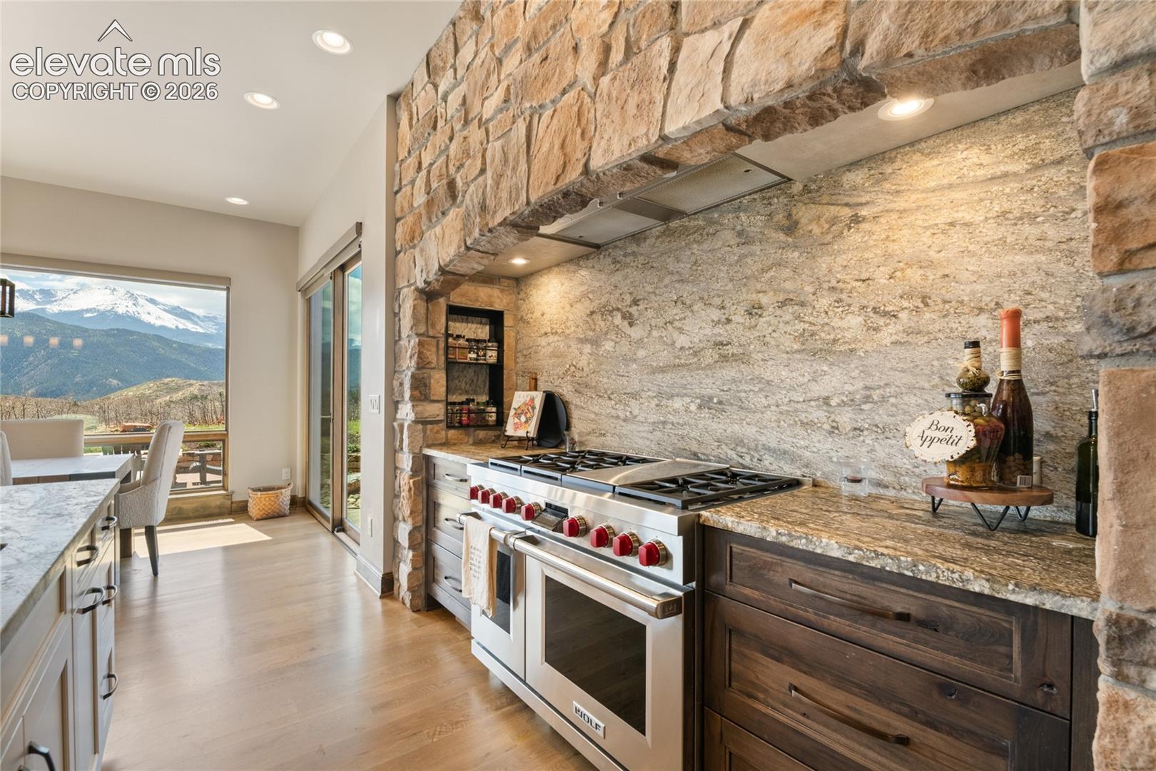 48-inch Wolf 6-burner range with griddle and double oven, framed by floor-to-ceiling stonework and full-slab granite backsplash.