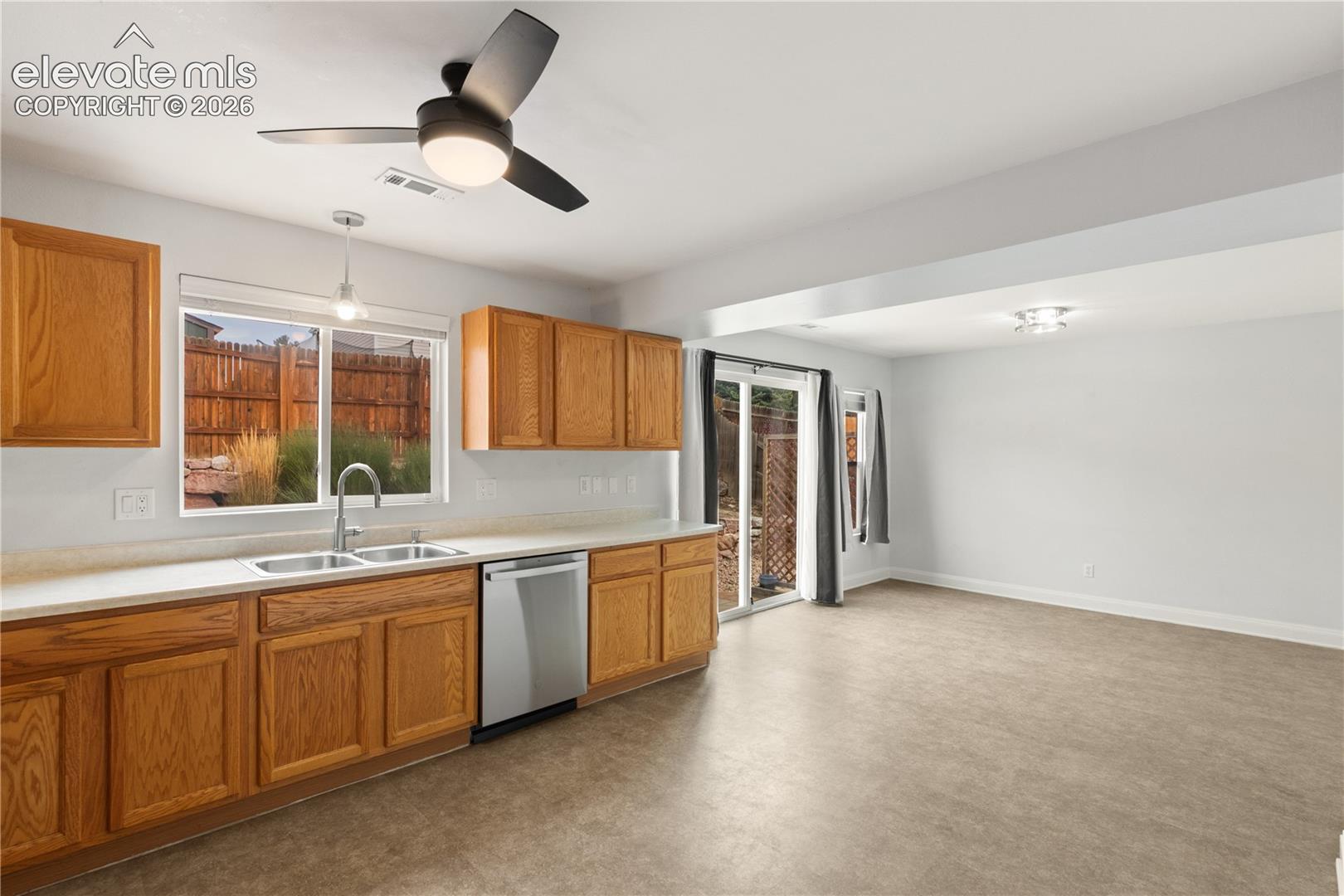Kitchen featuring wood cabinetry, solid surface countertops, stainless steel dishwasher, double-basin sink, and overhead ceiling fan with integrated lighting