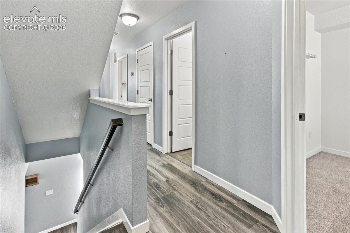 Wood-finish flooring, staircase with a modern black handrail, ceiling-mounted light fixture, and white trim accents