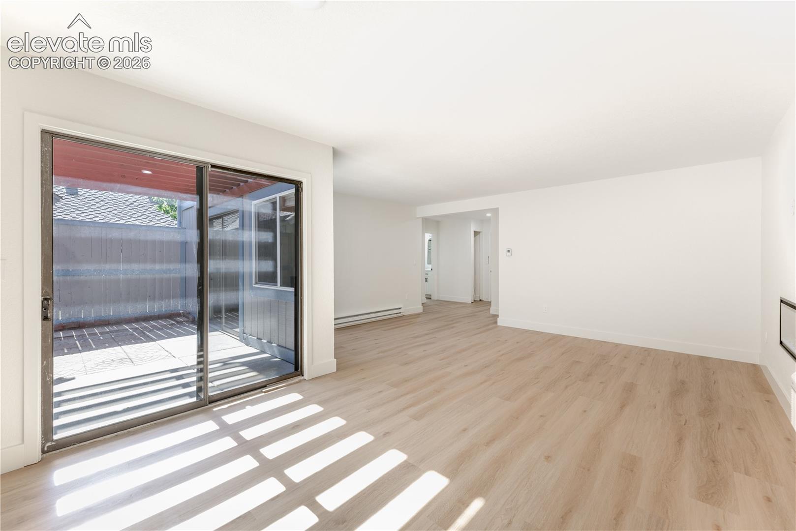 Living area featuring wood-finish flooring, smooth ceilings, and sliding glass doors opening to a concrete patio