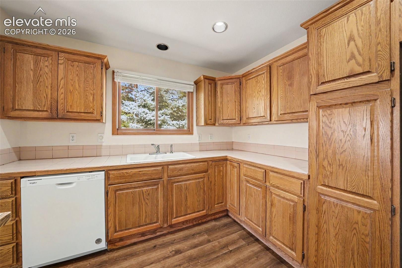 L-shaped kitchen with new LVP flooring, ample cabinetry, and an integrated white sink