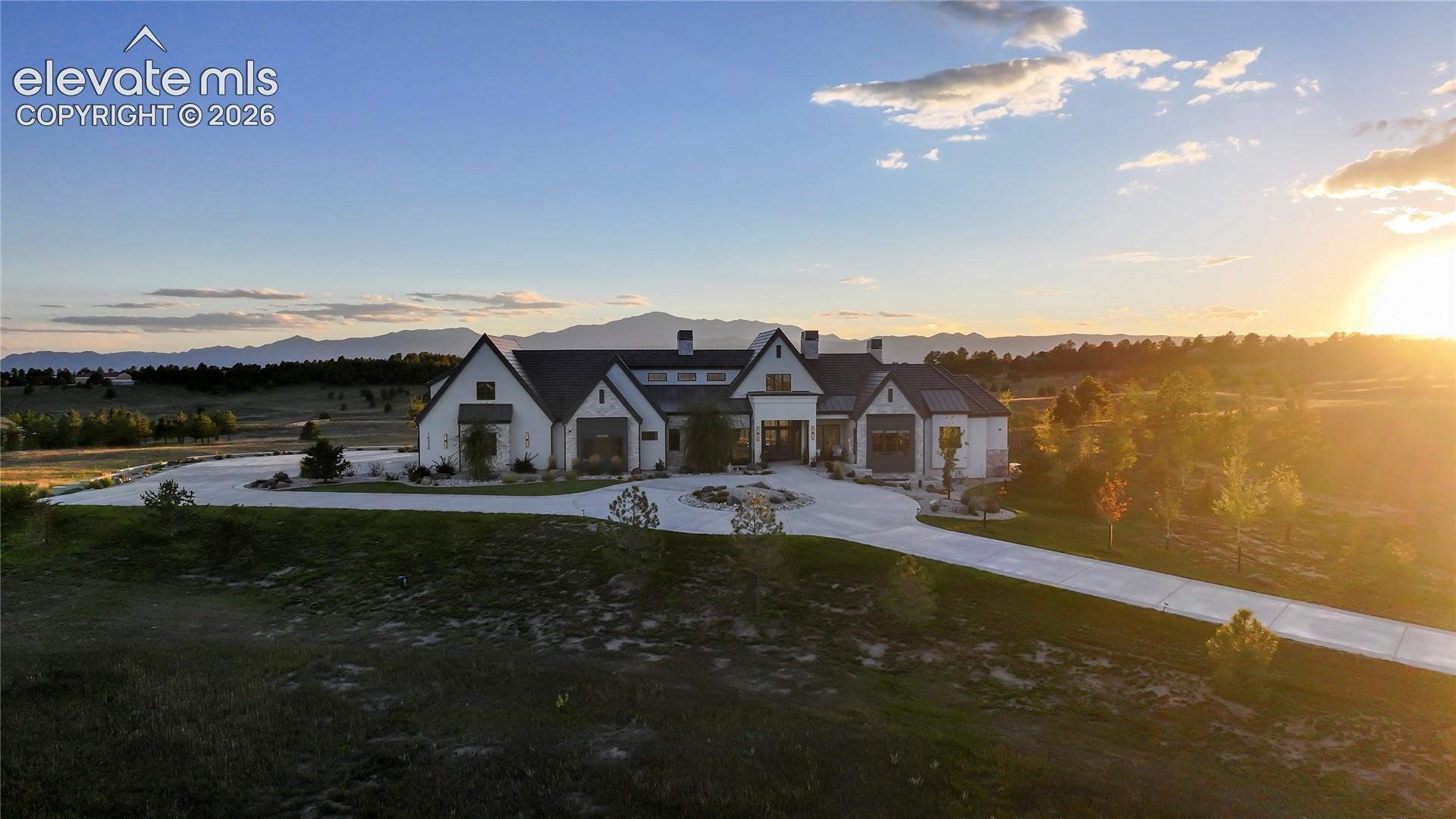 Multi-gabled estate featuring a light-toned exterior, steep rooflines, a circular motor court, concrete driveway, and expansive mountainous horizon