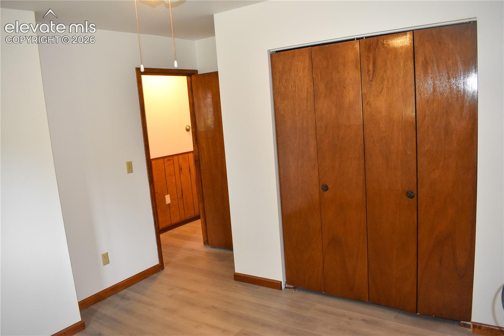 Light wood-finish flooring, white painted walls, wood trim, and a built-in closet with bi-fold doors