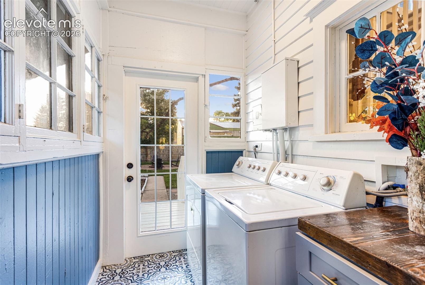 Bright utility area featuring a glass-paned exterior door, multiple casement windows, patterned floor tiling, and beadboard paneling