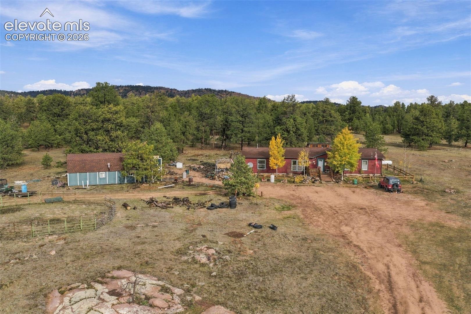 Expansive acreage featuring a residential structure with red exterior siding, a secondary detached building, timbered grounds, and mountain terrain
