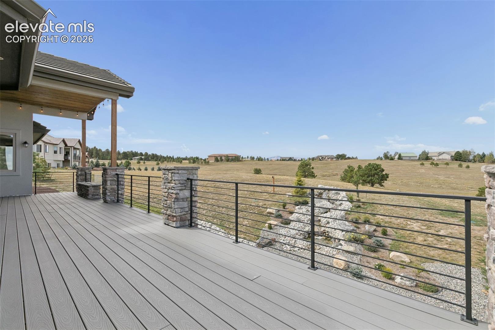 Expansive outdoor deck with composite decking, cable railing, and stone-clad pillars, featuring a covered patio area