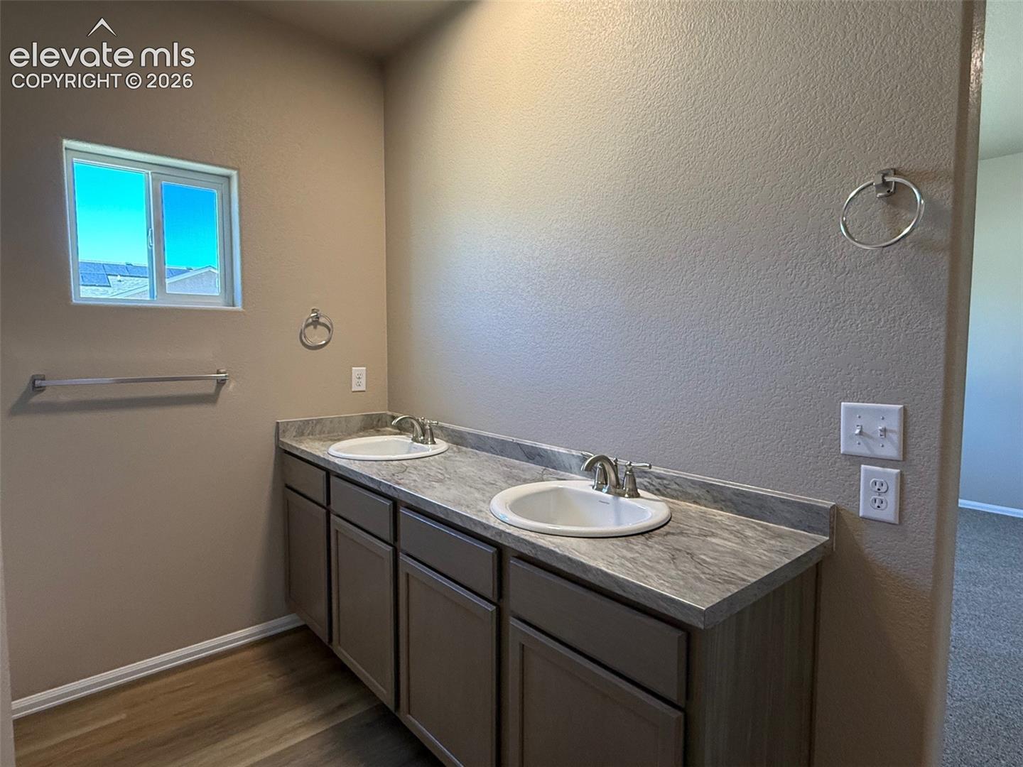 Double vanity with integrated sinks, brushed nickel faucets, wood-finish flooring, and a window for natural light