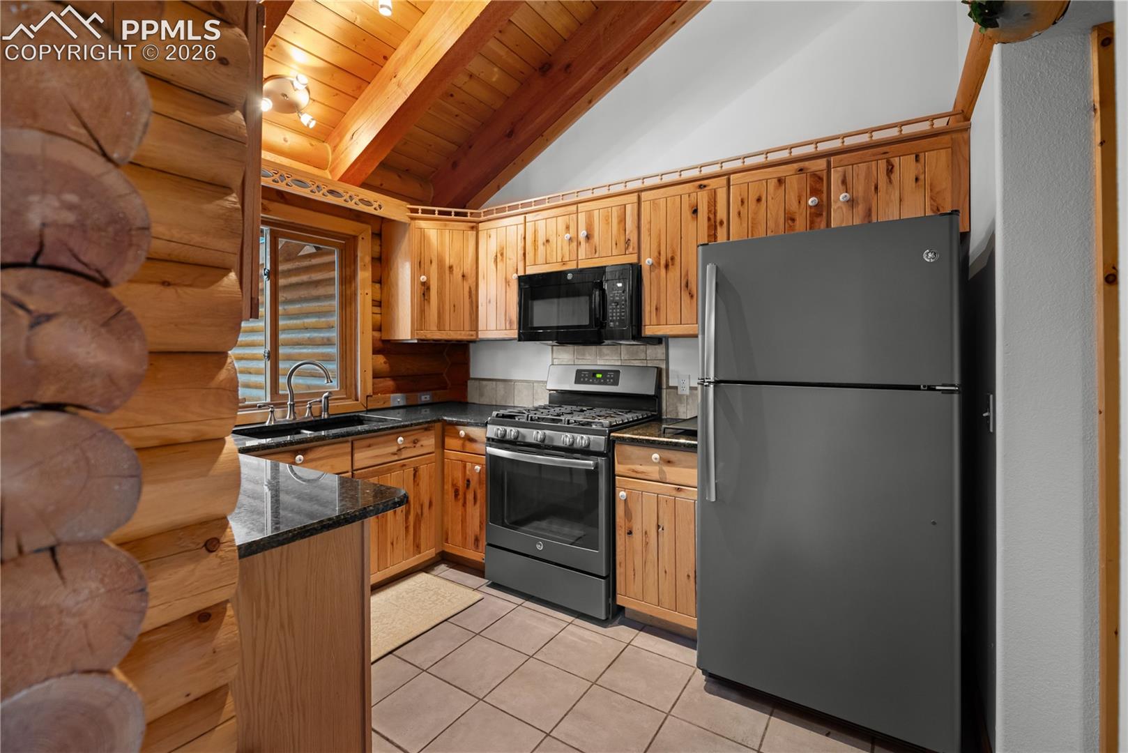 Kitchen with freestanding refrigerator, stainless steel range with gas cooktop, black microwave, wood ceiling, and light tile patterned floors