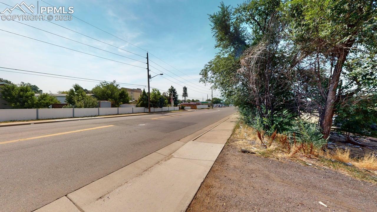 View of asphalt road featuring sidewalks, street lights, and curbs