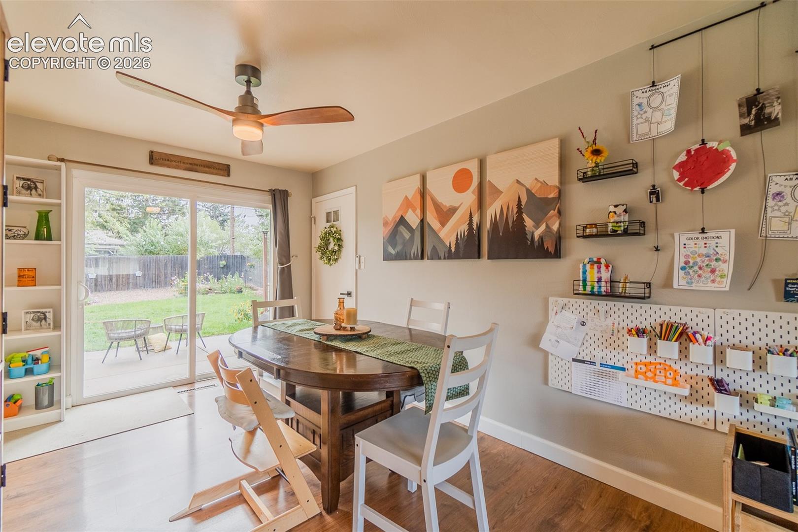 Sliding glass door, built-in shelving unit, wood-finish flooring, and ceiling fan with integrated lighting