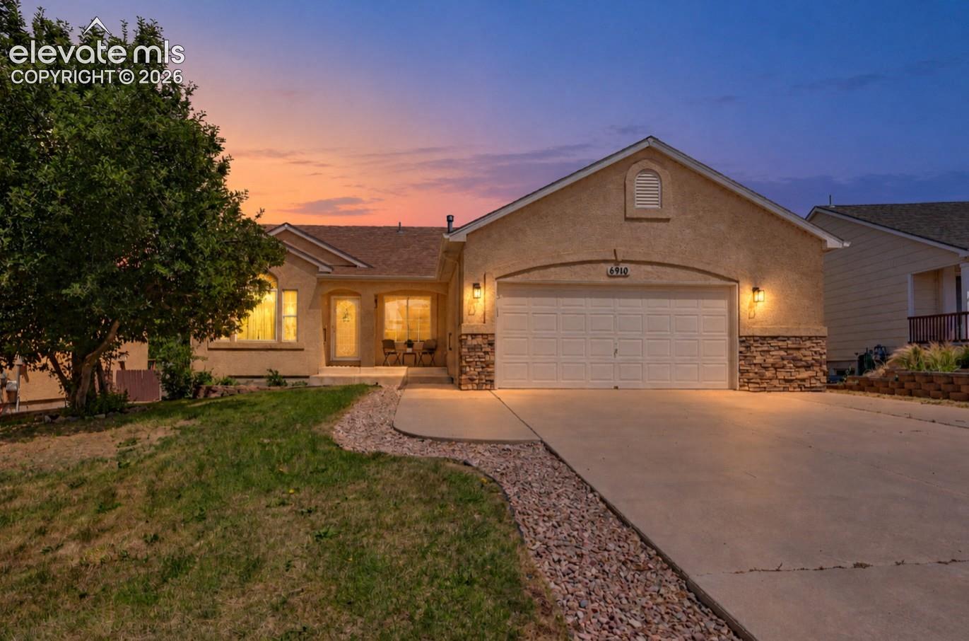 Single-story exterior featuring a stucco finish, stone veneer accents, an attached two-car garage, and a concrete driveway