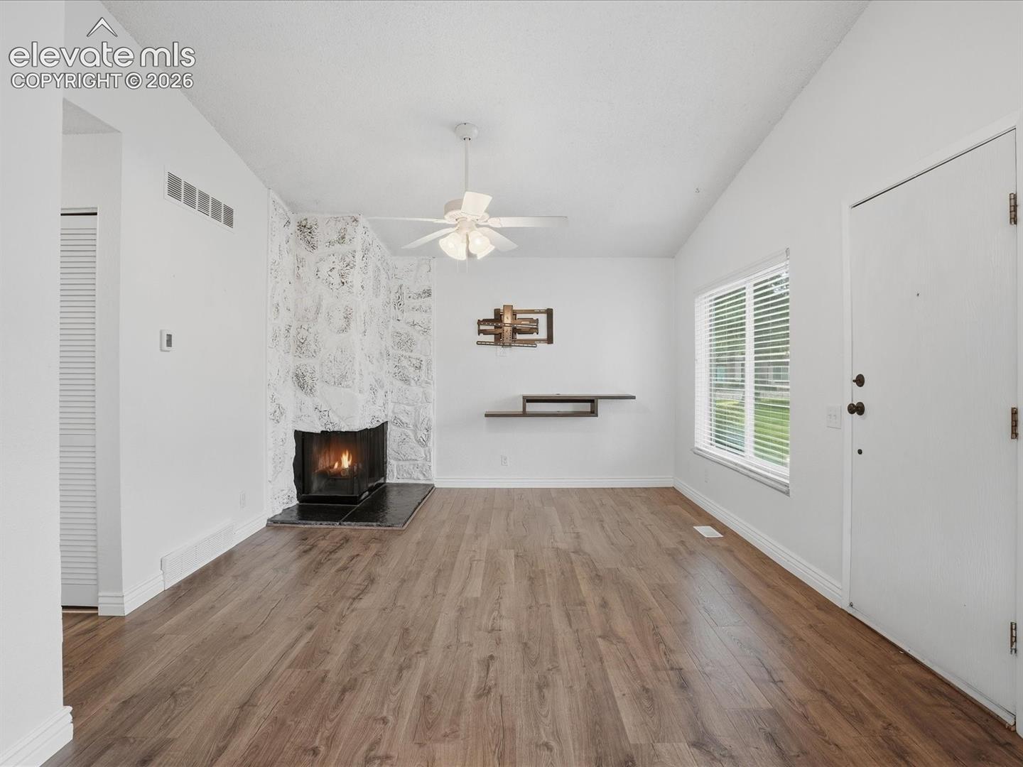 Vaulted ceilings, wood-finish flooring, stone-faced fireplace with a tile hearth, and a multi-blade ceiling fan with integrated lighting