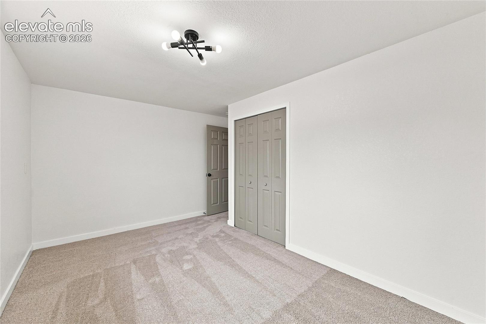 Neutral-toned carpet flooring, white painted walls, a flush-mount ceiling light fixture, a paneled door, and bi-fold closet doors