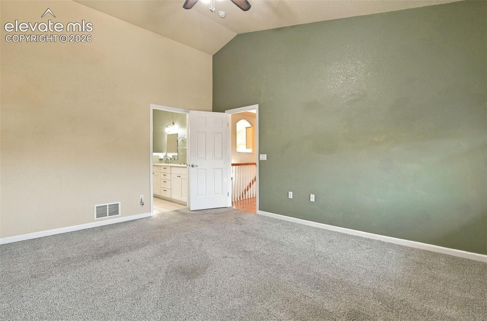 Vaulted ceilings with a ceiling fan, neutral wall finishes, and carpeted flooring