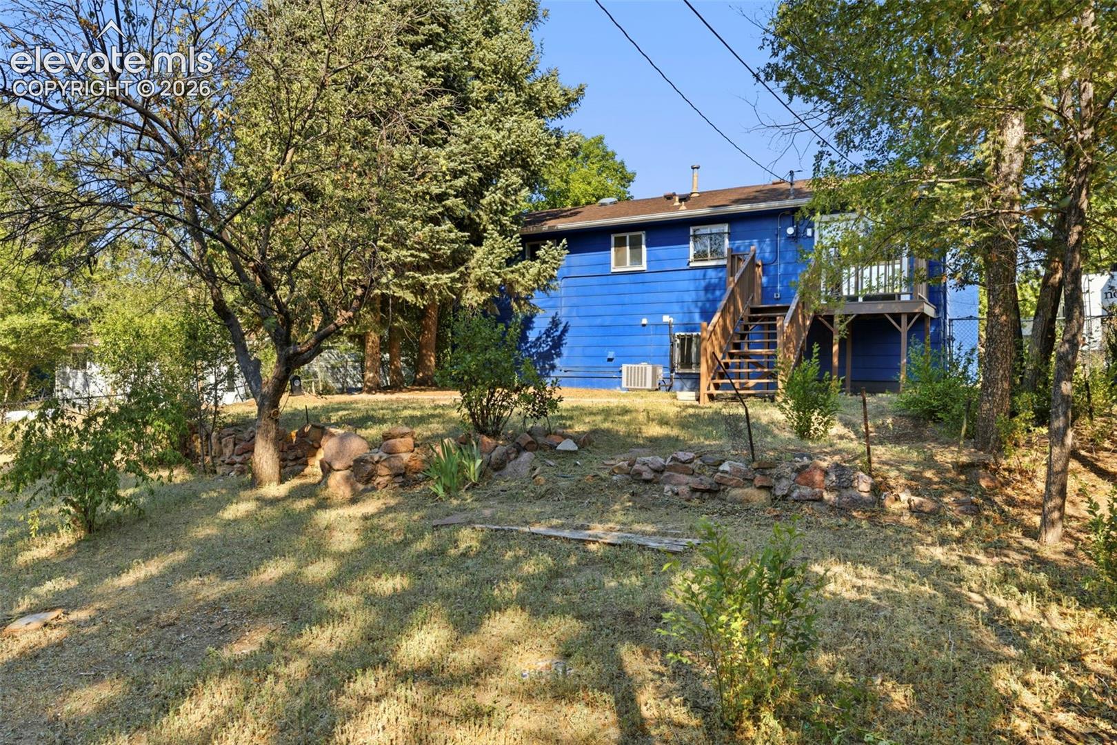 Split-level residence featuring a vibrant blue exterior, a rear wood deck, and an exterior staircase