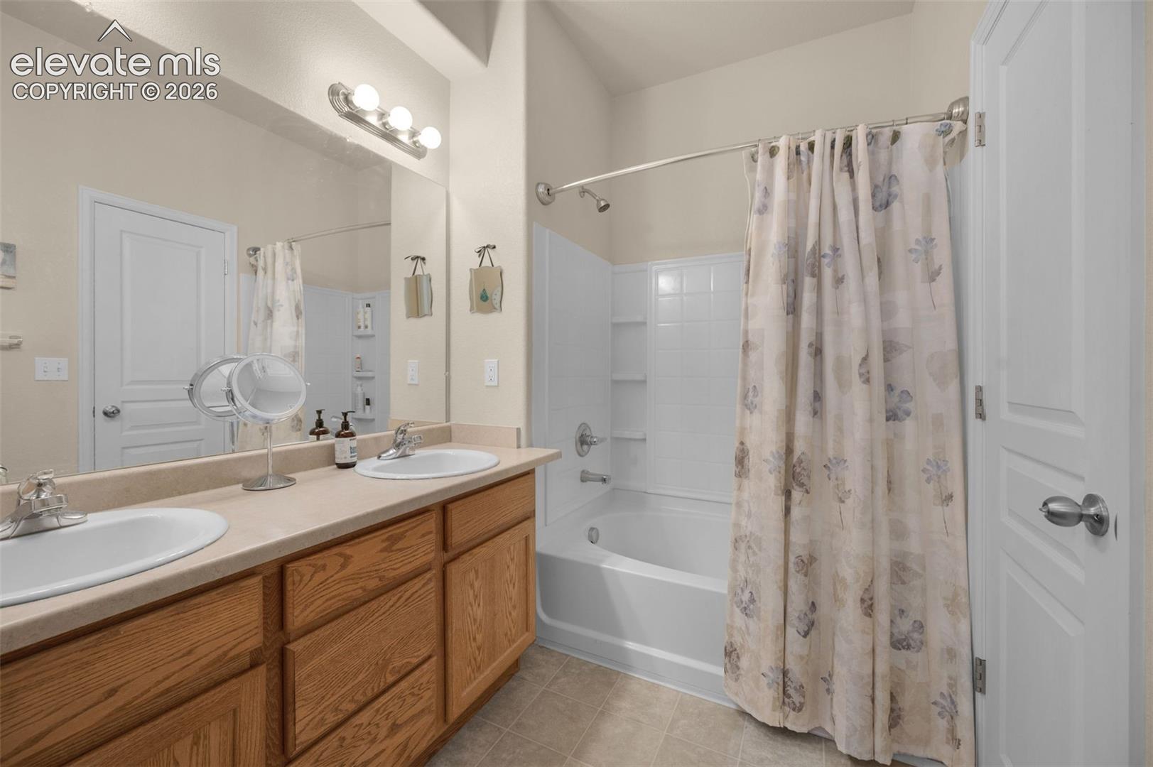 Dual basin vanity with wood-finish cabinetry, a large wall-mounted mirror, and a full-size bathtub with integrated shelving
