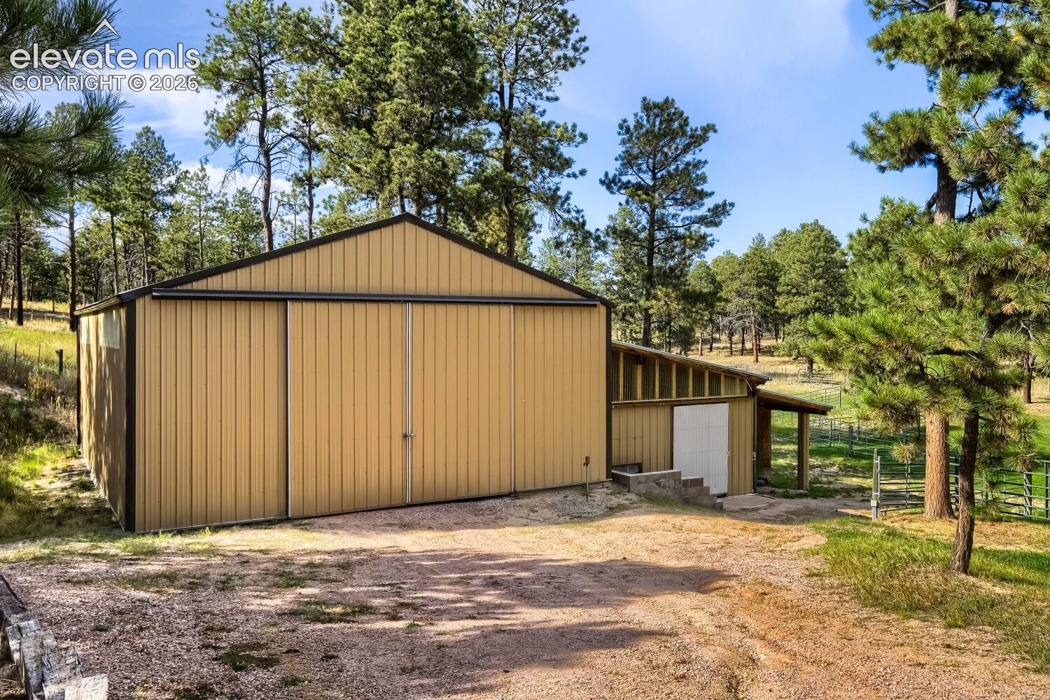 Metal-sided barn structure with a gabled roof, large sliding doors, and an attached lean-to shed with an overhang