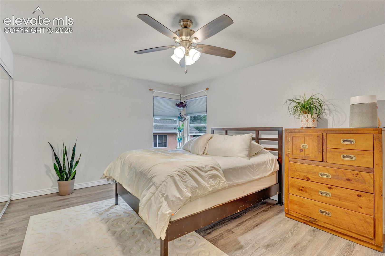 Bedroom featuring wood-finish flooring, a corner window, and a ceiling fan with integrated lighting