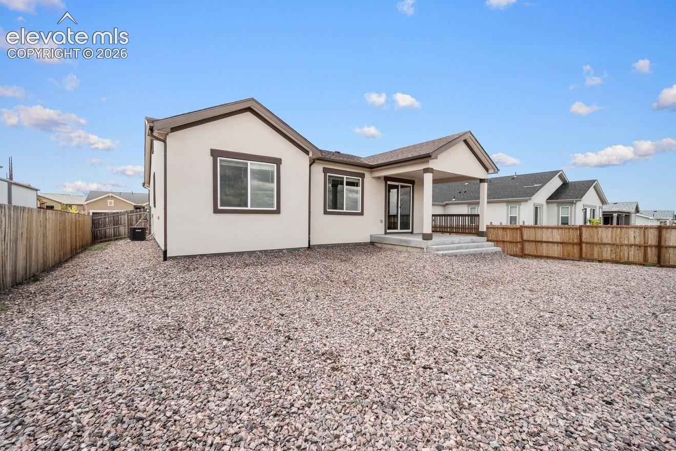 Single-story stucco exterior with a covered patio, fenced yard, and a gravel-covered ground