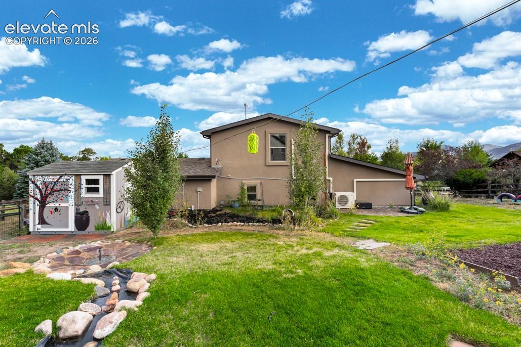 Spacious backyard featuring a manicured lawn, a decorative dry creek bed, and an outbuilding with a painted exterior