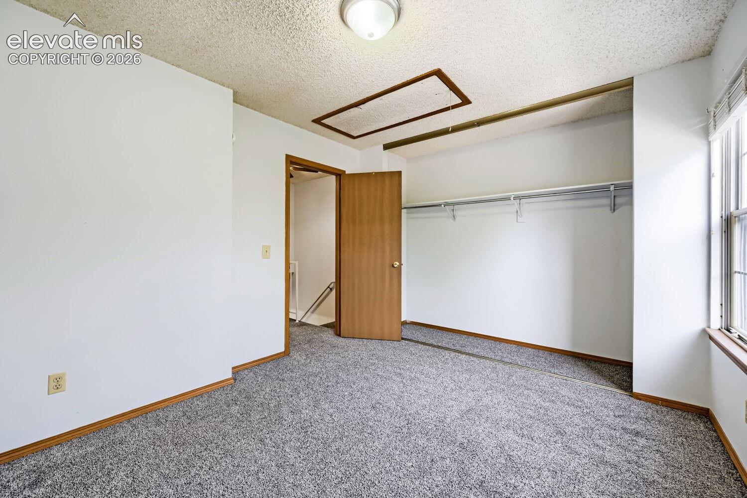 Wall-to-wall carpeting with light-toned trim, a built-in closet with hanging rod, and a window providing natural light