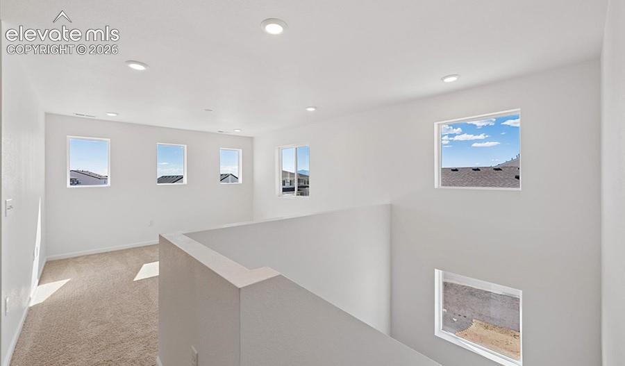 Open loft area featuring neutral carpeting, recessed ceiling lighting, and multiple windows