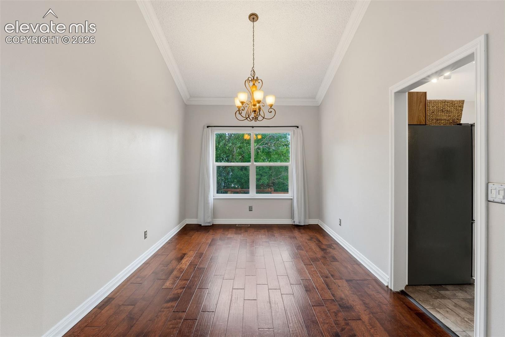 Elegant formal dining room showcasing rich wood-finish flooring in a herringbone pattern, crisp white walls and ceiling with crown molding, a brass multi-arm chandelier, and abundant natural light from a large multi-pane window framing mature greenery