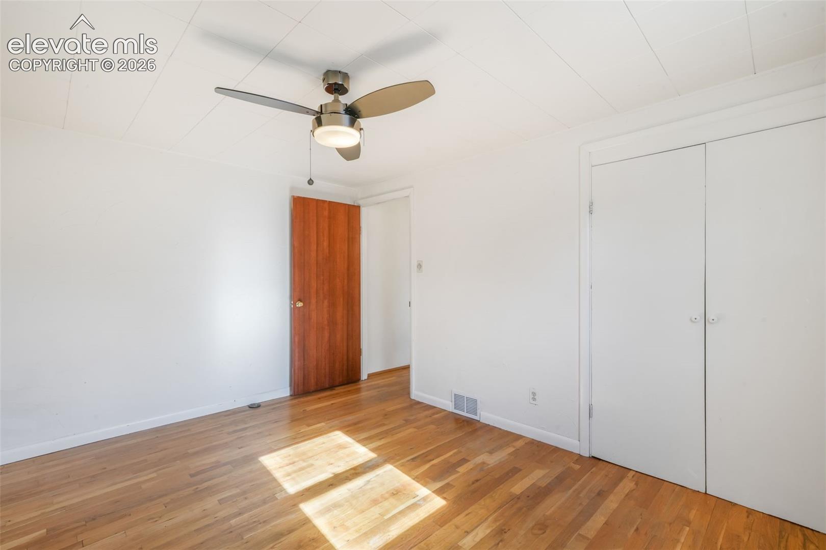 Wood-finish flooring, white walls, and a ceiling fan with integrated lighting