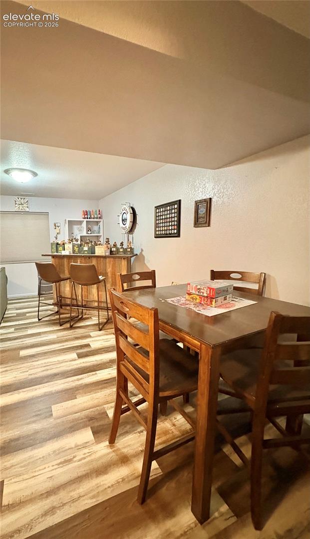 Wood-finish flooring, built-in bar with shelving, recessed lighting, and a square dining table