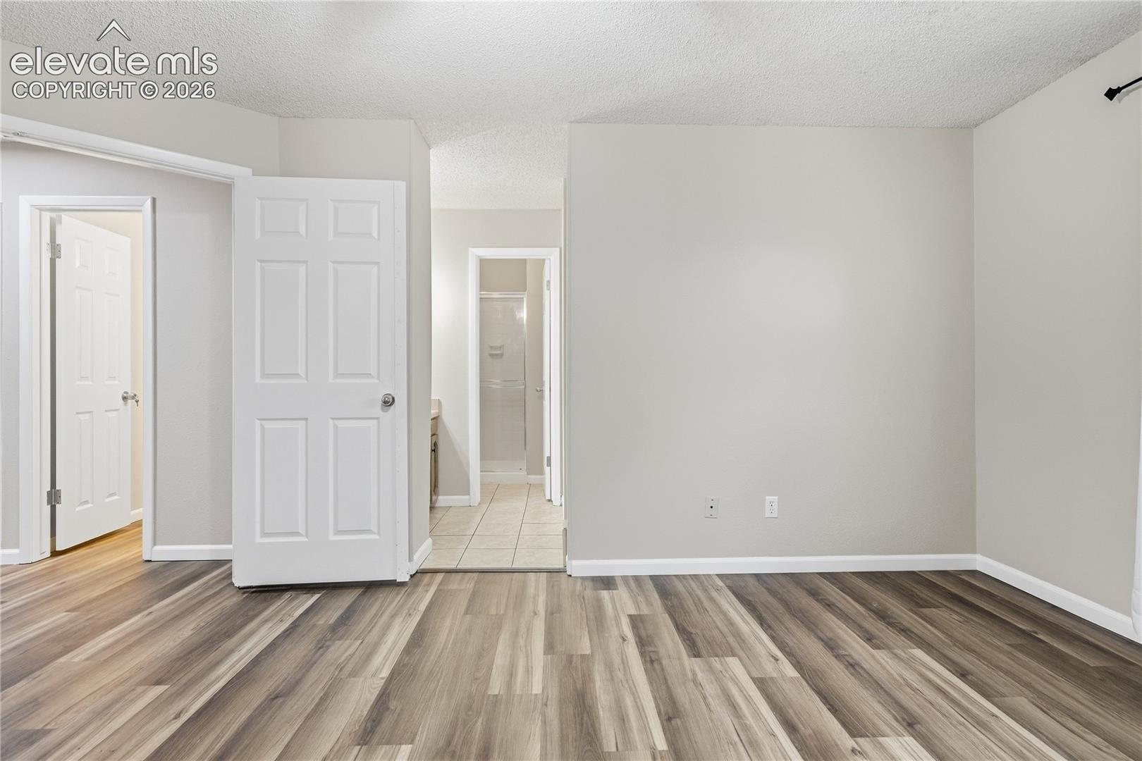 Wood-finish flooring, light neutral wall paint, white trim, and white paneled doors