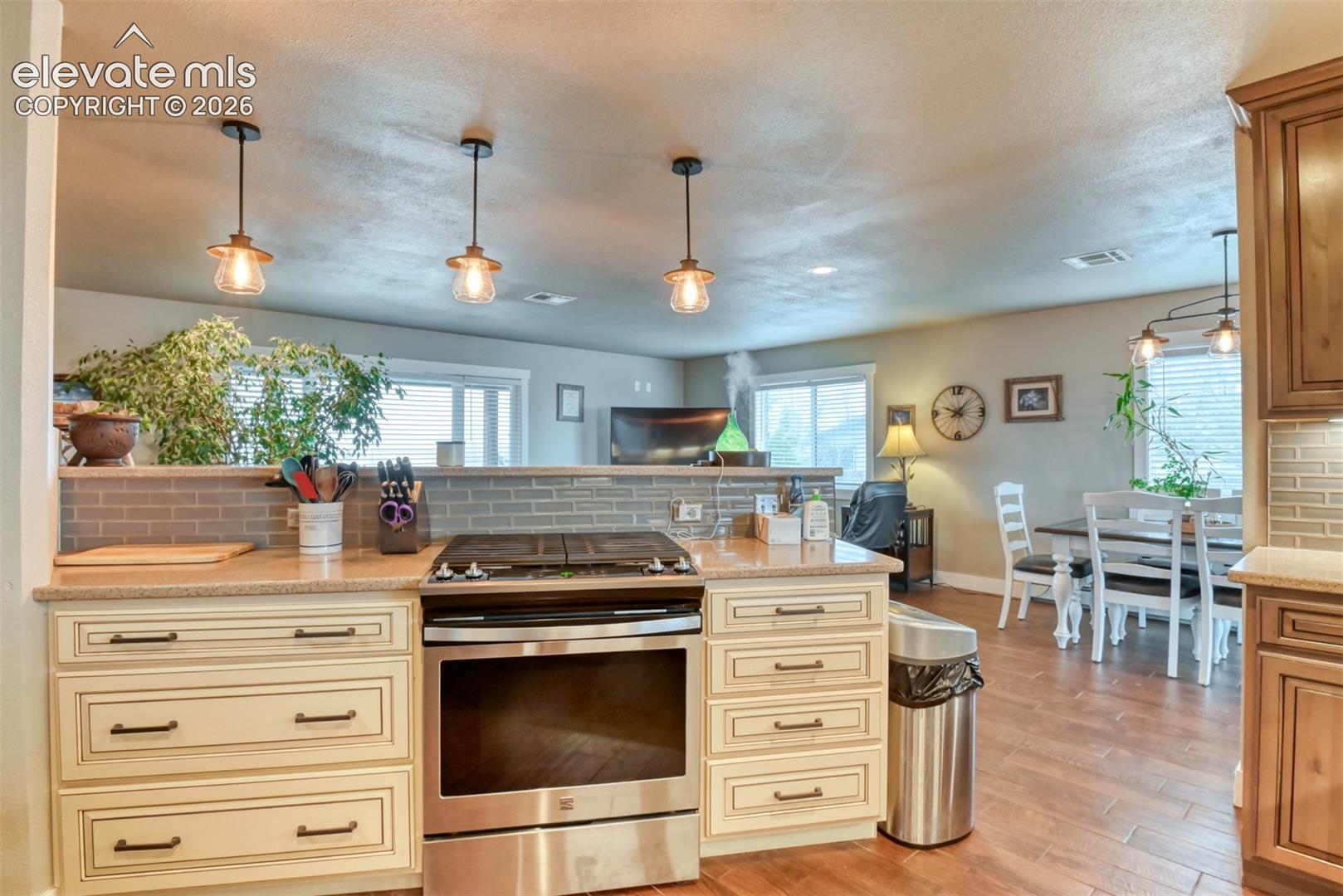 Kitchen featuring cream cabinetry, decorative backsplash, stainless steel gas range oven, and pendant lighting