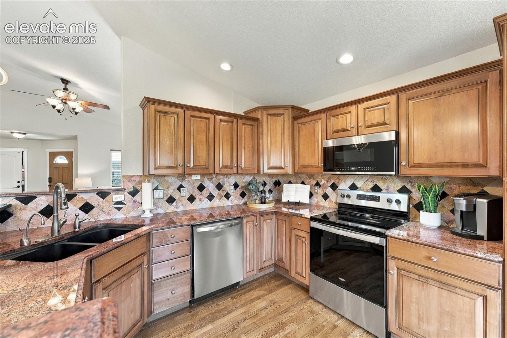 Kitchen featuring wood cabinetry, stone countertops, diamond-pattern tile backsplash, stainless steel appliances, and wood-finish flooring