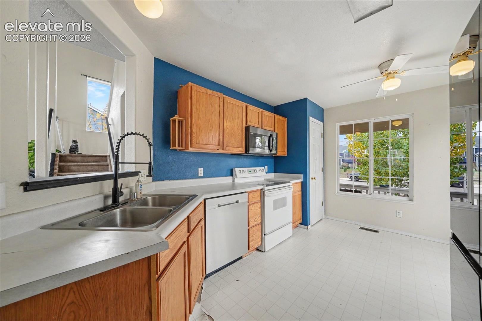 Kitchen featuring natural wood cabinetry, stainless steel dishwasher and microwave, matte black gooseneck faucet, and white countertops