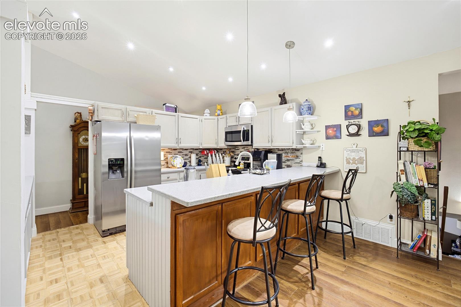 Kitchen featuring white upper cabinetry, a central island with wood-finish base and light-toned countertop, stainless steel refrigerator, and wood-finish flooring