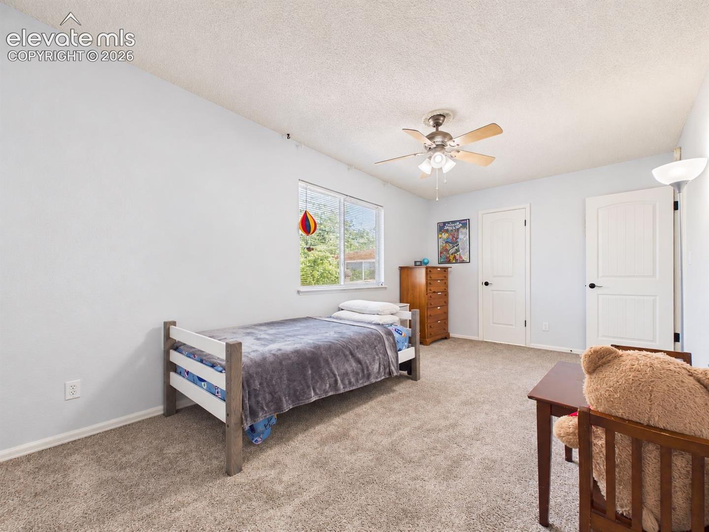 Another view highlights the bedroom's ample floor space, natural light, ceiling fan, and flexible layout for furniture placement.