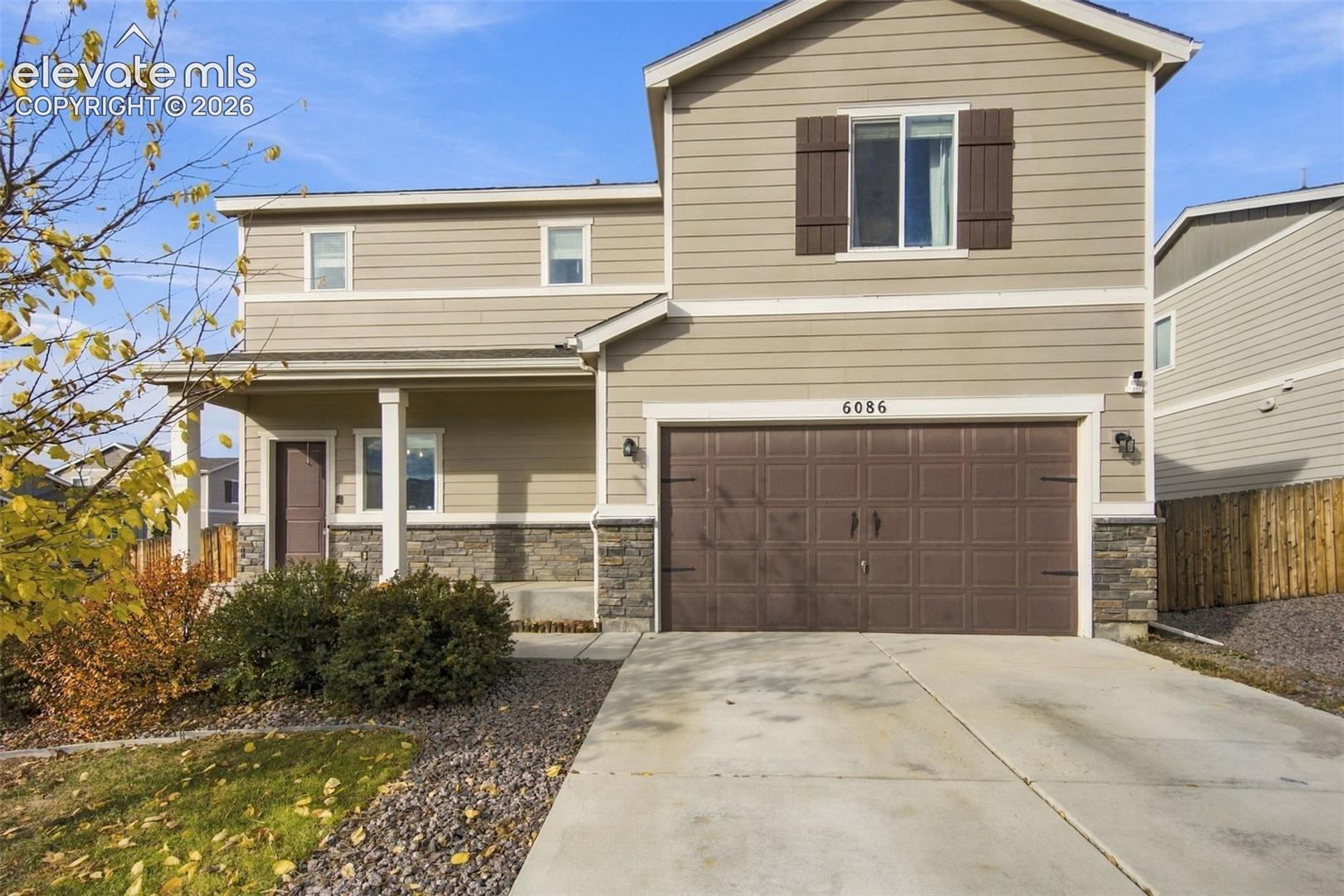 Two-story exterior featuring horizontal siding, stone veneer accents, a covered front porch, and a two-car garage