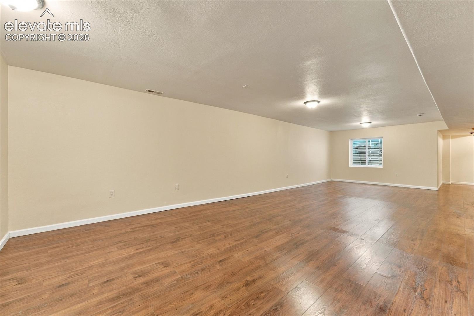 Expansive interior space featuring wood-finish flooring, neutral wall paint, and multiple flush-mount ceiling lights