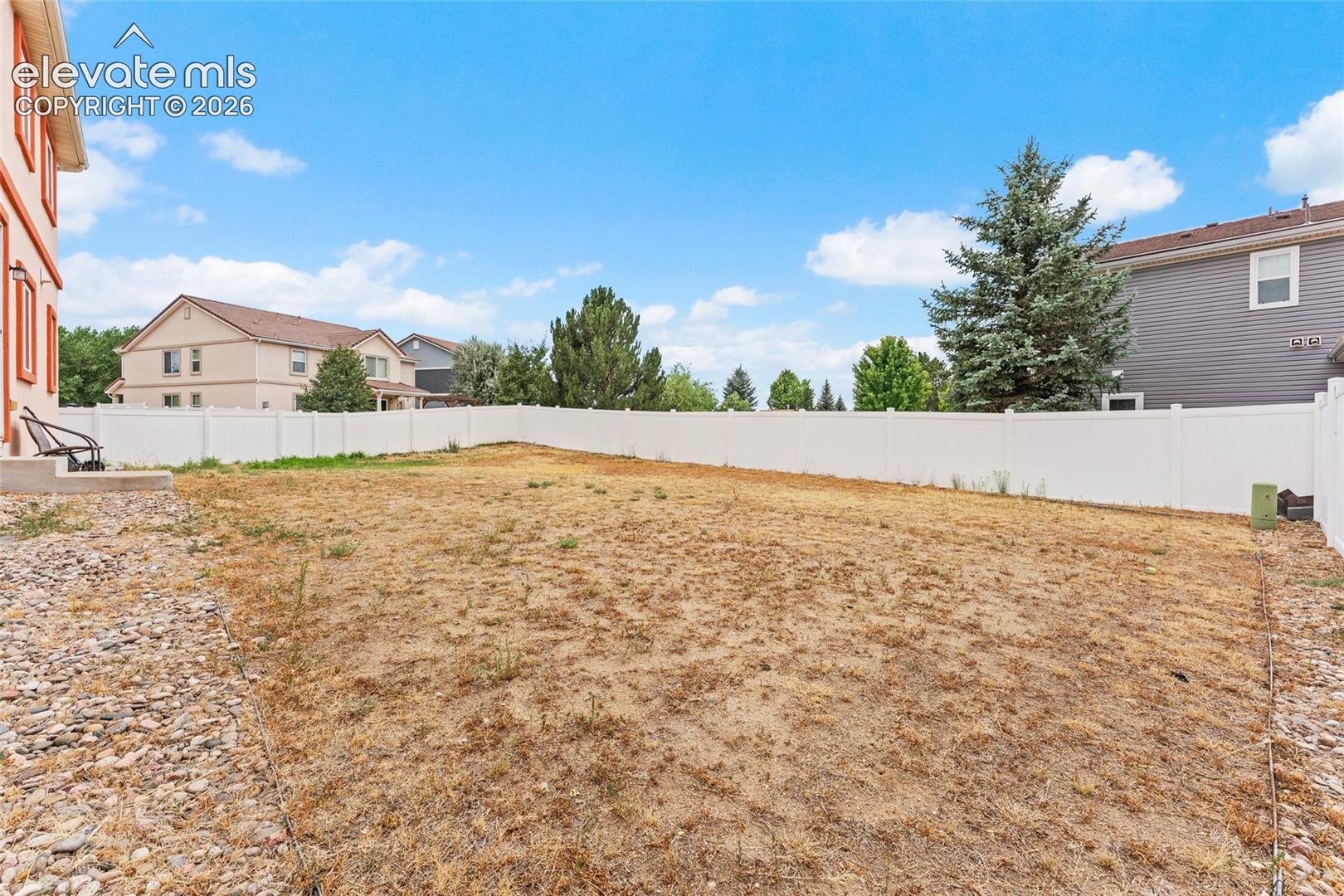 Backyard featuring a white vinyl privacy fence and stone-mulched perimeter borders