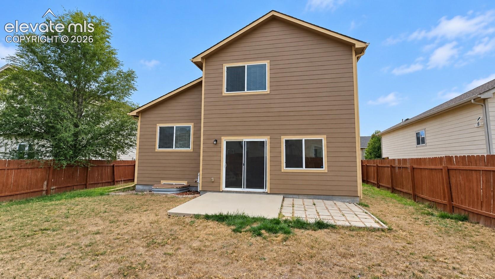Two-story residence featuring horizontal lap siding, a rear sliding glass door, a concrete patio, and a wood privacy fence enclosing the backyard