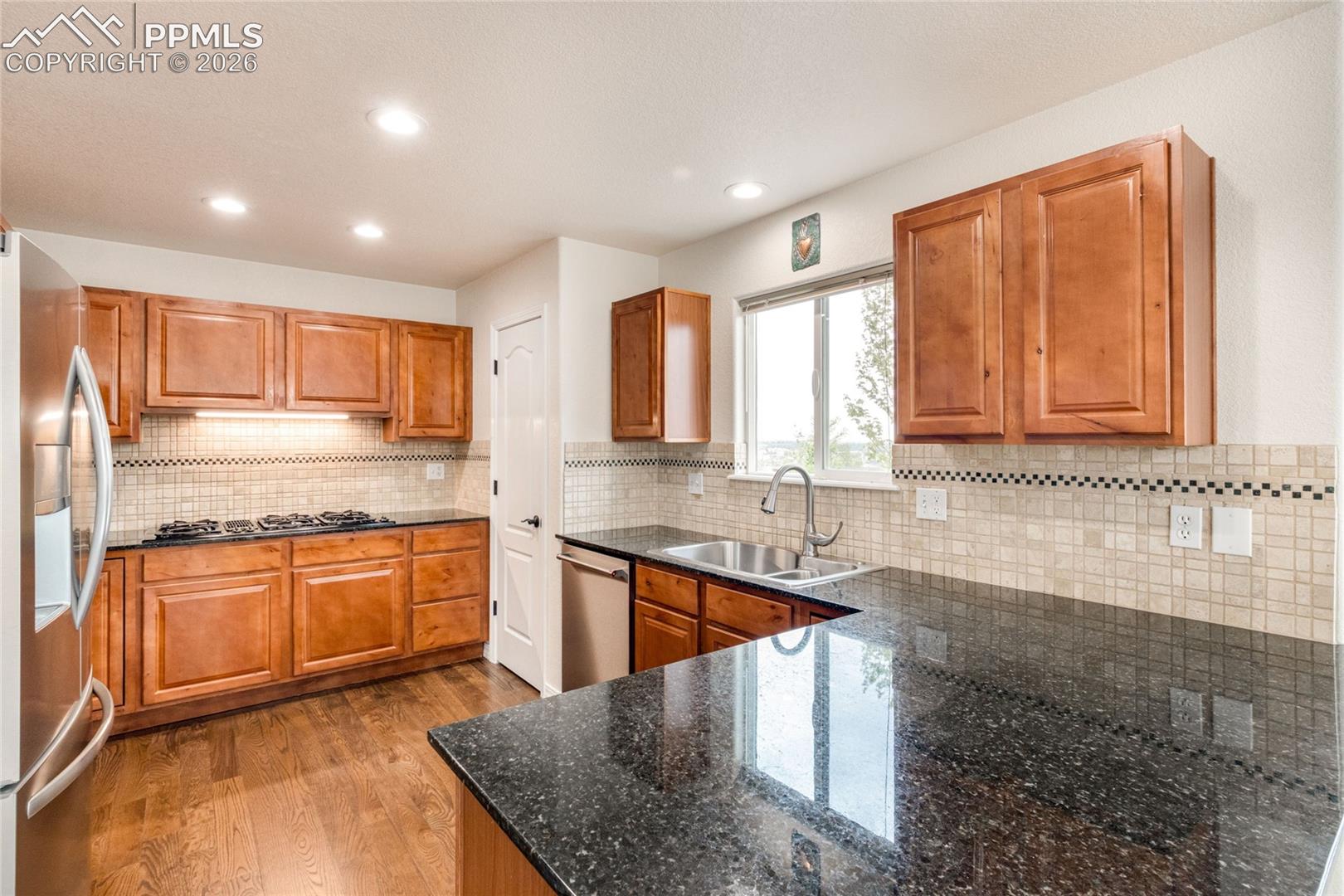 Kitchen featuring rich wood cabinetry, dark speckled countertops, GenAir cooktop, and a tiled backsplash
