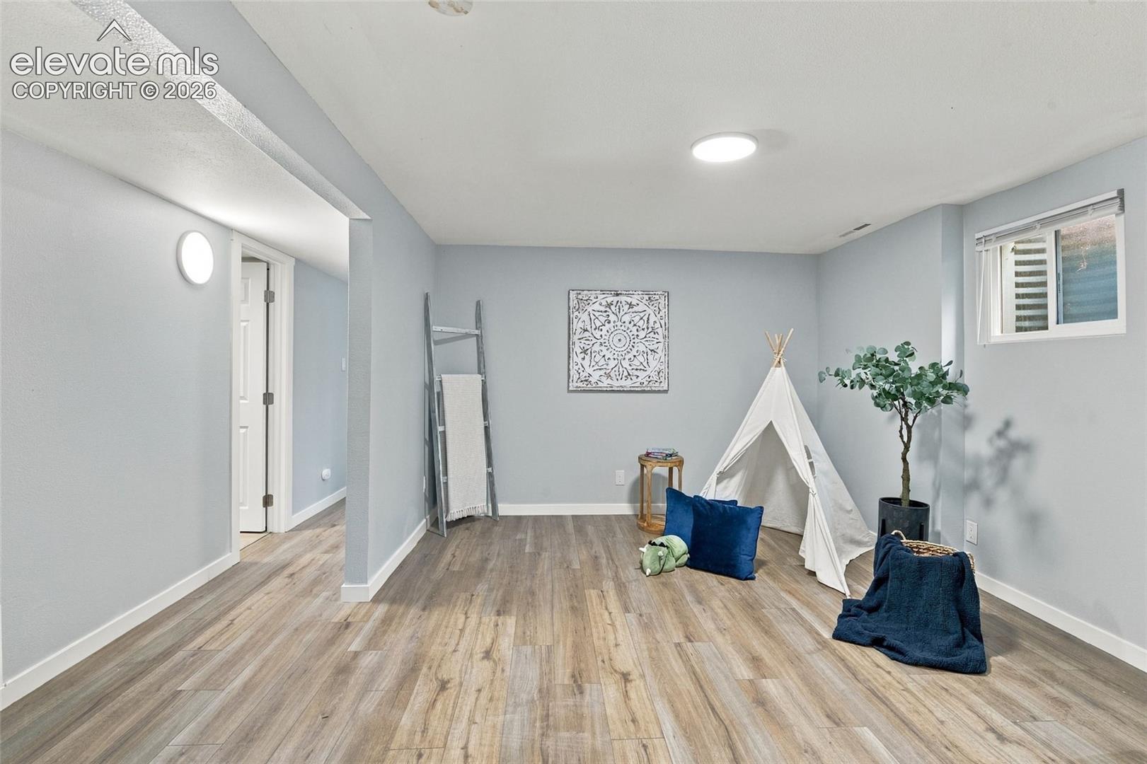 Neutral-toned interior space featuring wood-finish flooring, recessed lighting, wall-mounted light fixtures, and a single-pane slider window