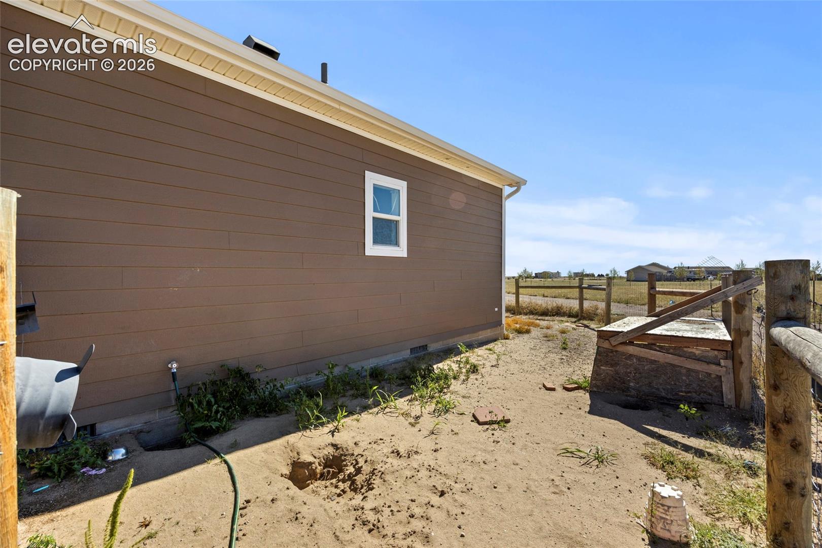 Exterior side elevation featuring horizontal lap siding, a single white-framed window, and a wooden post-and-rail perimeter fence