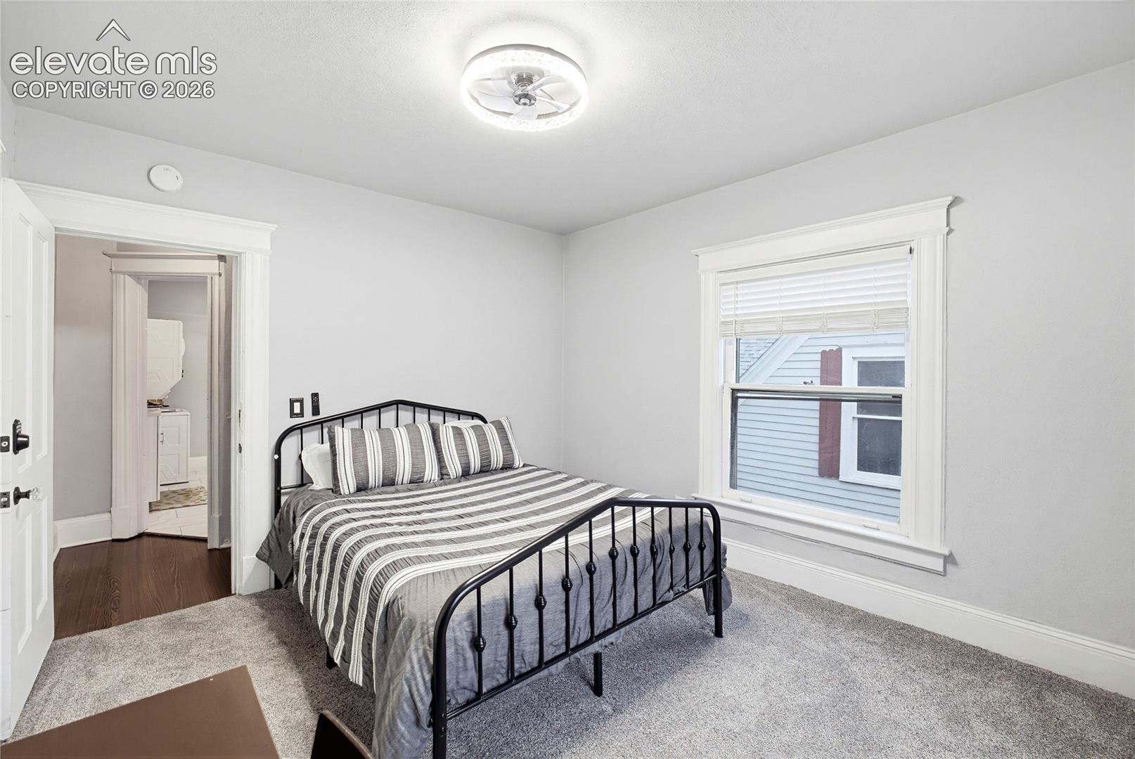 Light gray wall color, carpeted flooring, white trim details, window with white blinds, and a ceiling-mounted light fixture
