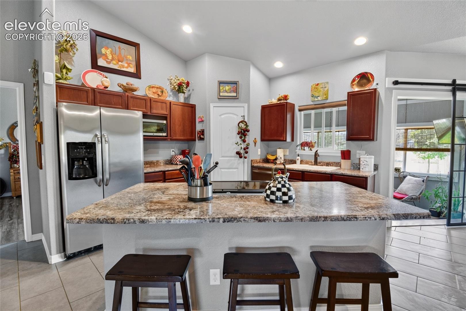 Kitchen featuring custom wood cabinetry, stone-finish countertops, a central island with a built-in cooktop, recessed lighting, and a sliding barn-style door