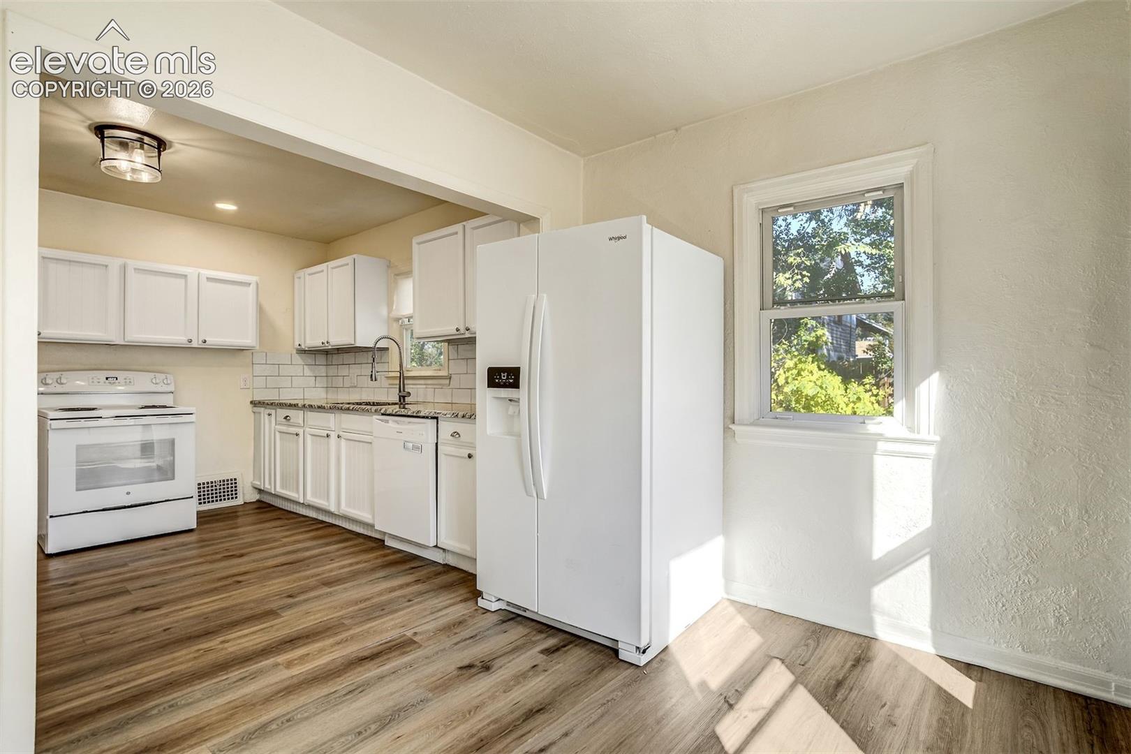 Kitchen featuring white cabinetry, wood-finish flooring, subway tile backsplash, and white appliances