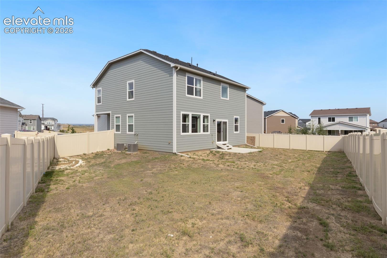 Expansive backyard featuring a new vinyl fence, concrete patio, and a two-story residence with gray siding and white-framed windows