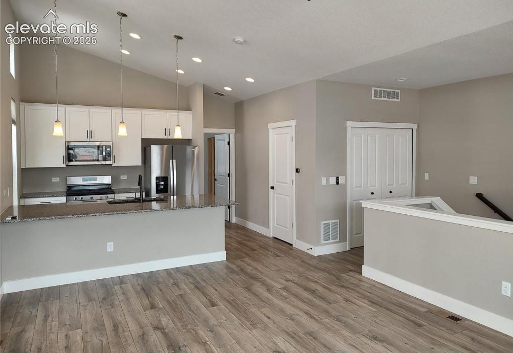 Kitchen featuring white cabinetry, stone countertops, stainless steel appliances, wood-finish flooring, and vaulted ceilings with recessed lighting